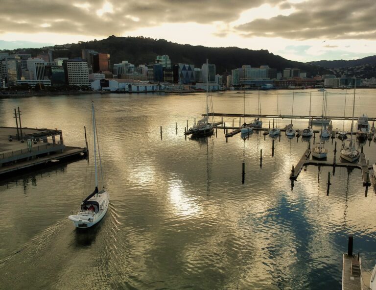 A yacht motoring into Chaffers Marina at sunset, with the Wellington city skyline behind